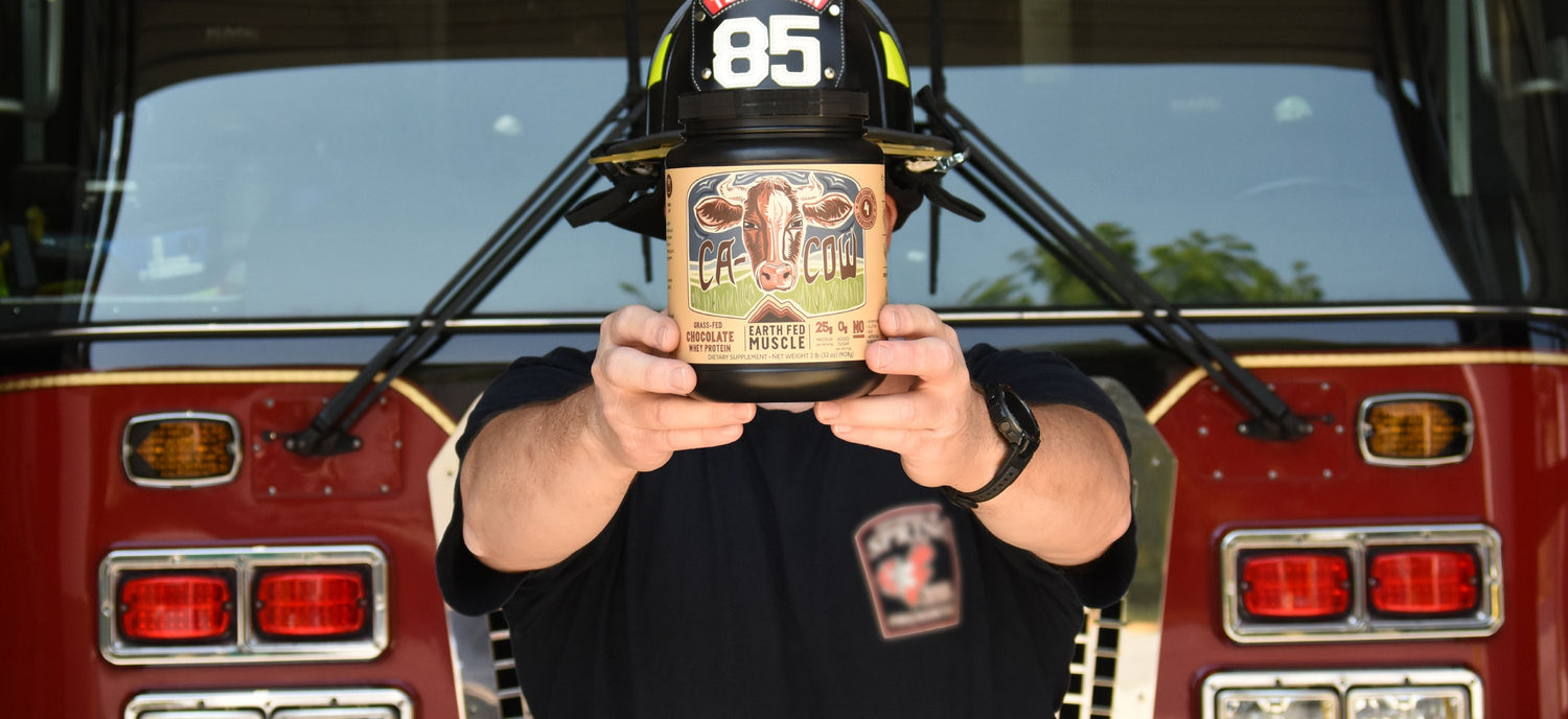 Firefighter standing in front of firetruck holding chocolate protein powder